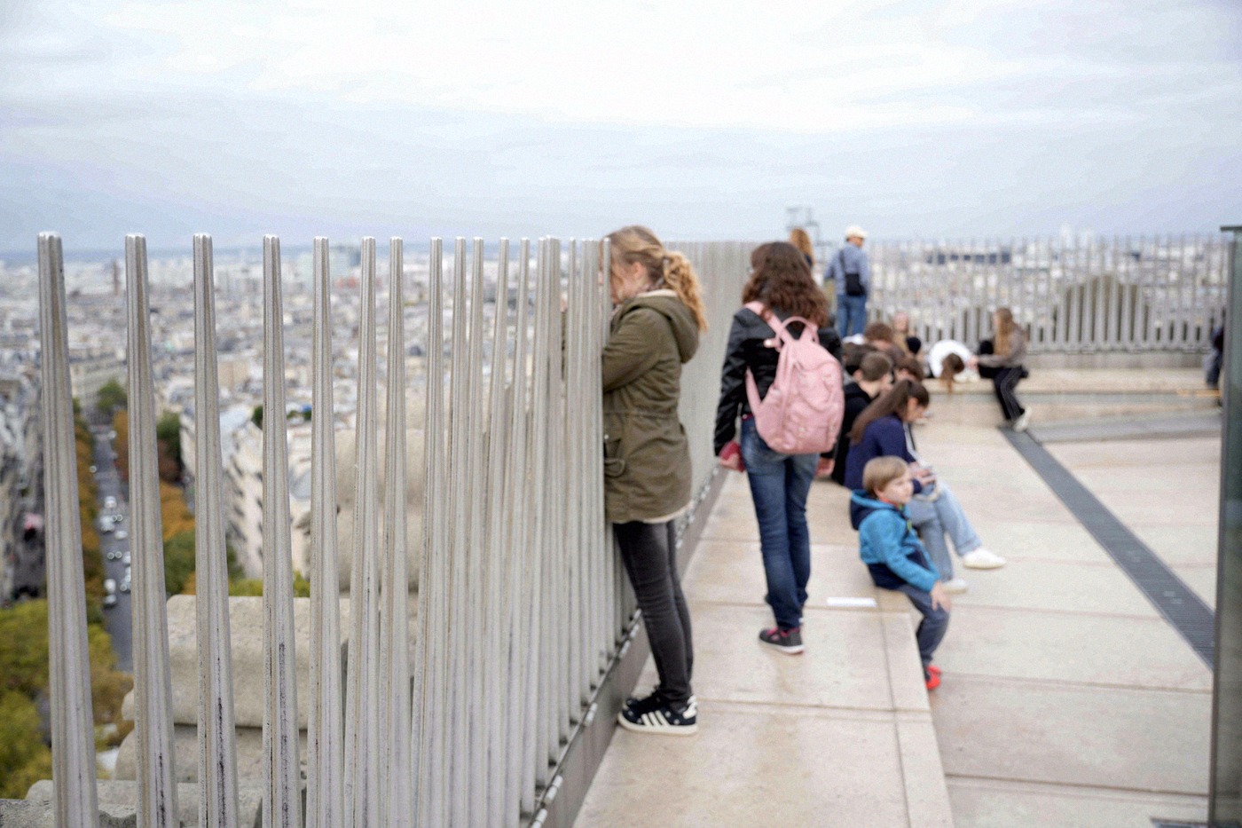 Tourists stand on the rooftop terrace of the Arc de Triomphe, enjoying the panoramic view over the Paris