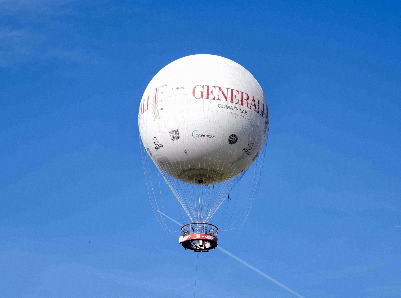 The white Generali Climate Lab tethered balloon floats over Paris against a brilliant blue sky.