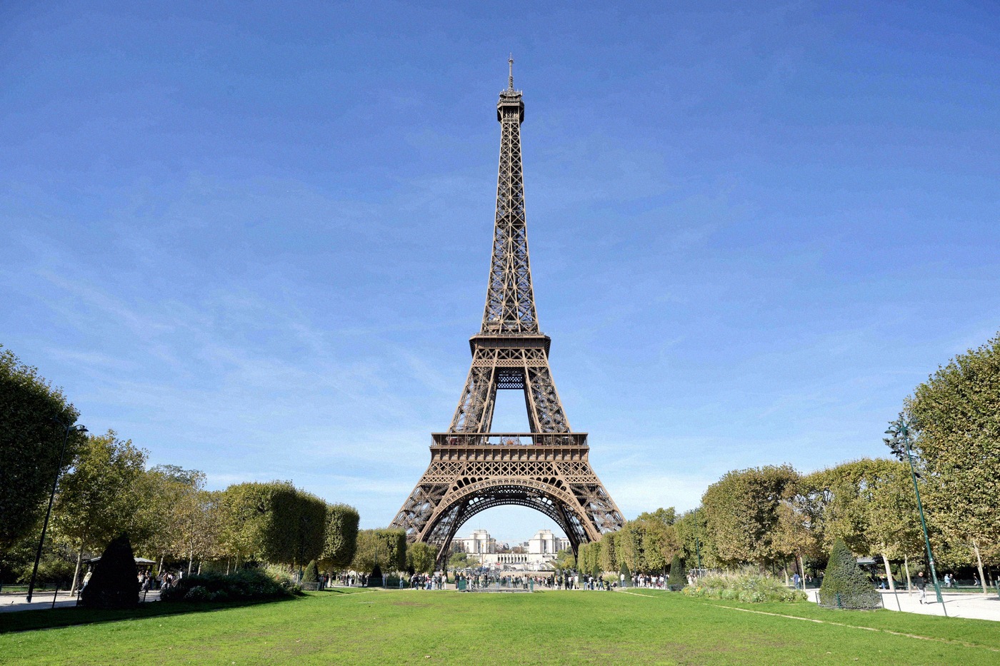 The Eiffel Tower rises against a brilliant blue sky above the green lawns of the Champ de Mars.