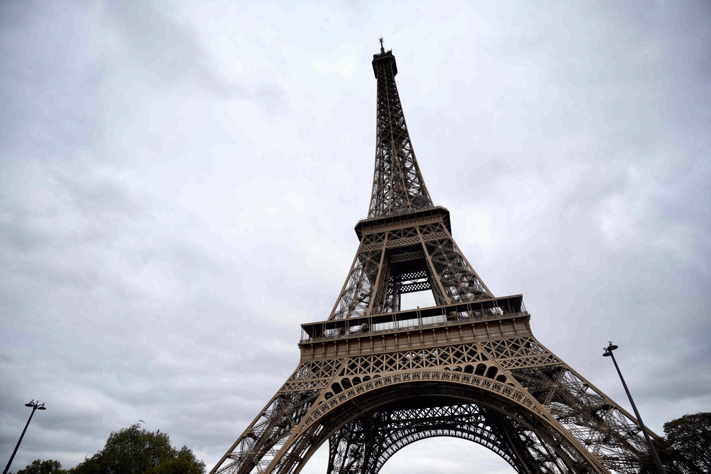 The Eiffel Tower shot from a dramatic low angle against a cloudy sky, its intricate iron lattice dominating