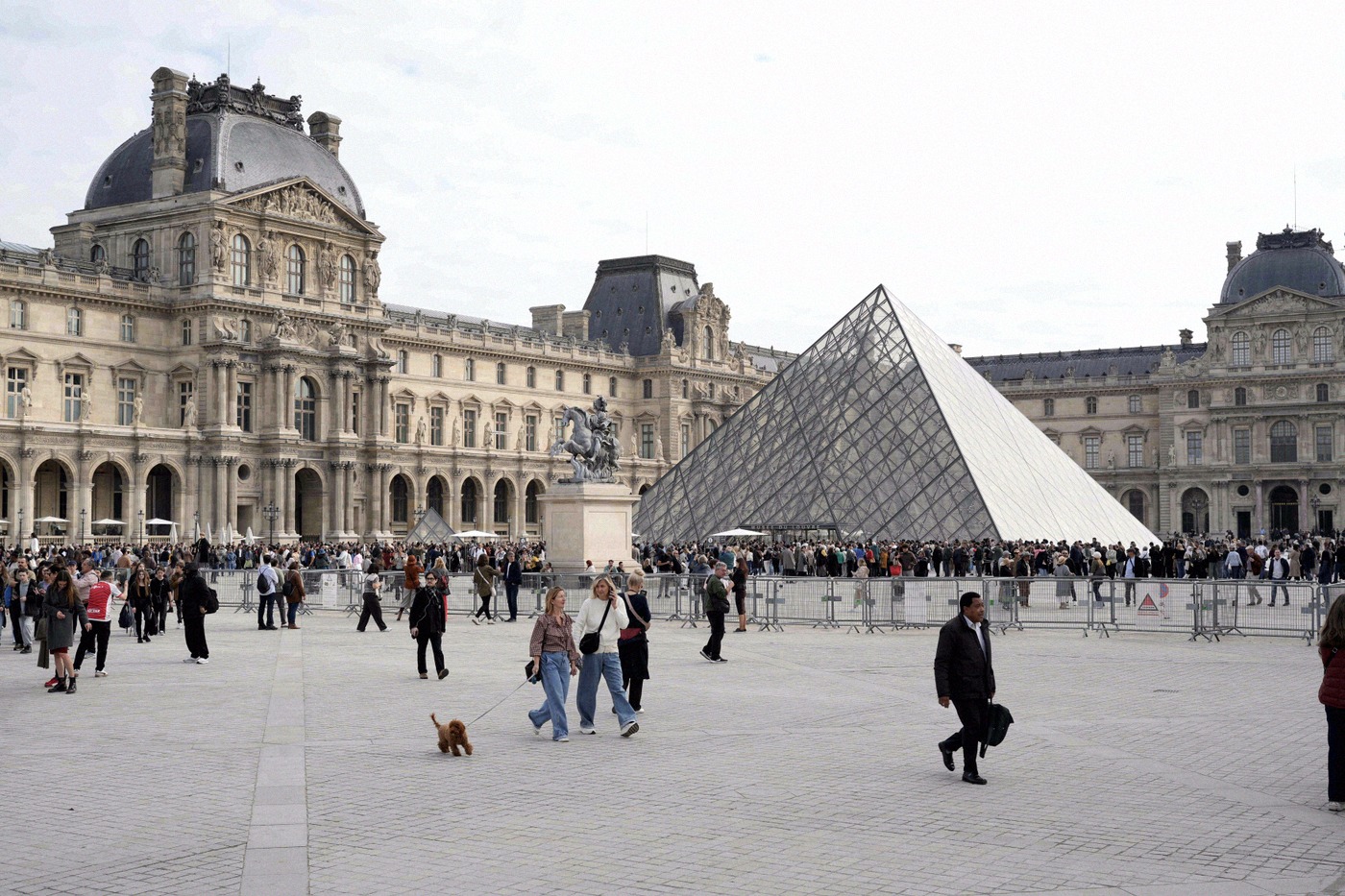 The Louvre's glass entrance pyramid towers over the Cour Napoléon, surrounded by crowds of visitors and the