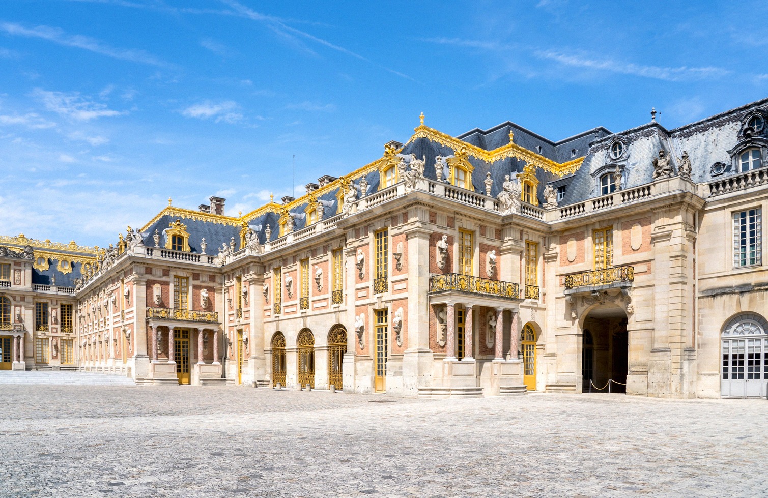 La façade baroque dorée de la cour de Marbre du château de Versailles, avec sa balustrade rouge et blanc.