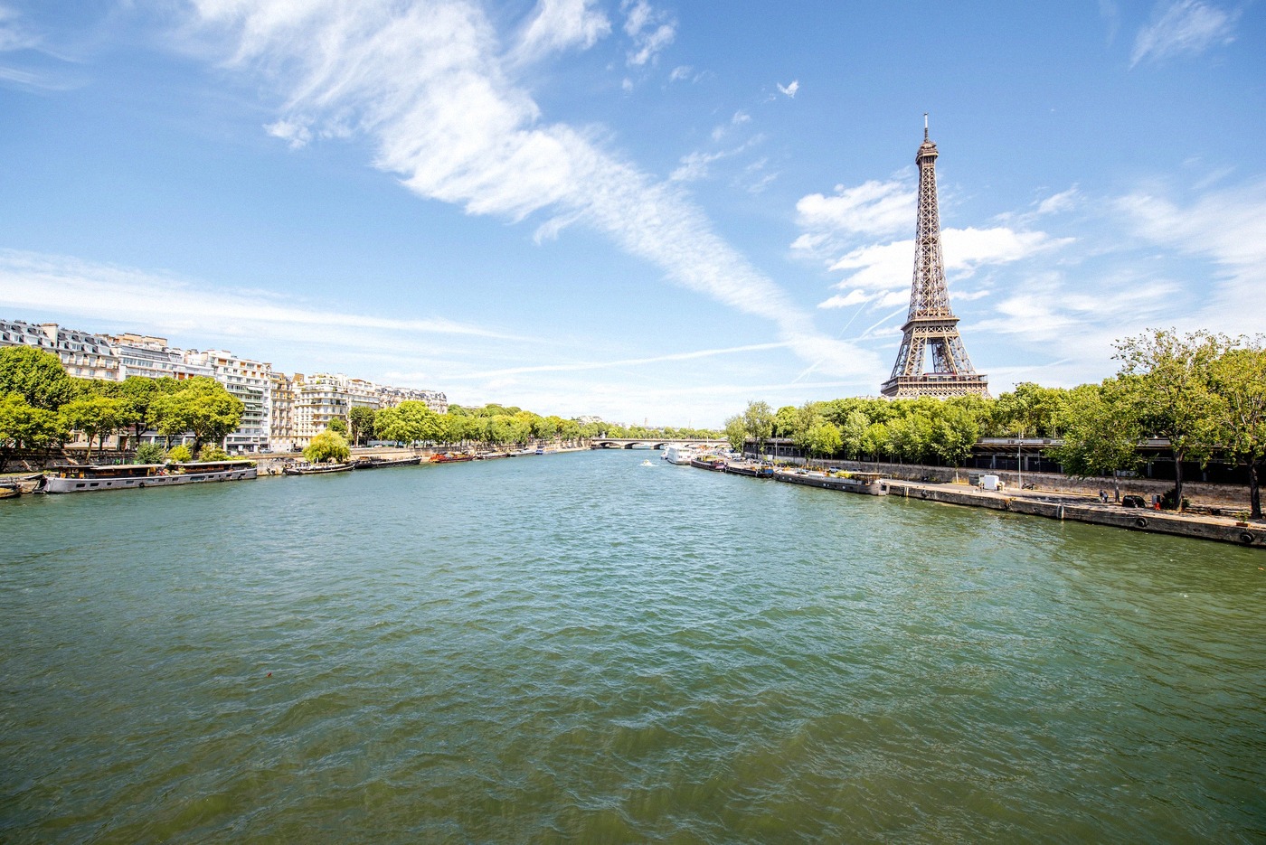 Vue grand angle de la Seine à Paris avec la tour Eiffel à l'arrière-plan à droite, des arbres verts le long des quais.